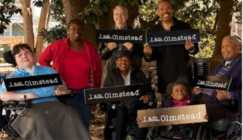 diverse group of people with disabilities holding i am Olmstead signs